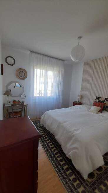 A cozy bedroom with a large bed, white bedding, soft lighting, a patterned rug, wooden furniture, mirrors, wall decor, and sheer curtains on the window.