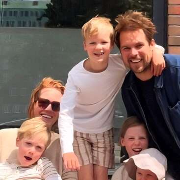 A happy family poses together outdoors on a sunny day. Four children surround their smiling parents. The mood is joyful, relaxed, and filled with warmth and laughter.