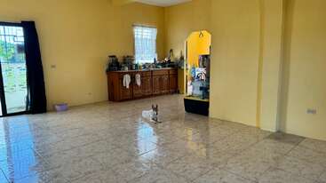 Ein kleiner Hund liegt auf dem glänzenden Fliesenboden in einem geräumigen Raum mit gelben Wänden, Küchenzeile, Holzschrank, Fenstern und wenigen Möbeln. Licht füllt den Raum.