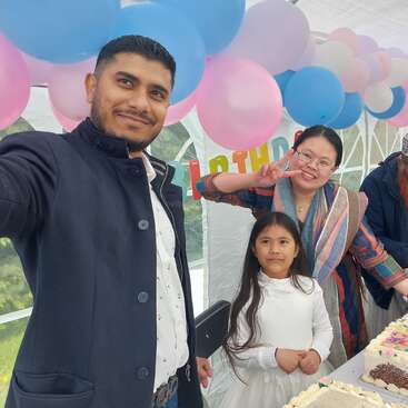 Un homme prend un selfie avec une femme et une petite fille lors d'une fête d'anniversaire. Des ballons colorés et des gâteaux créent une ambiance joyeuse et festive.