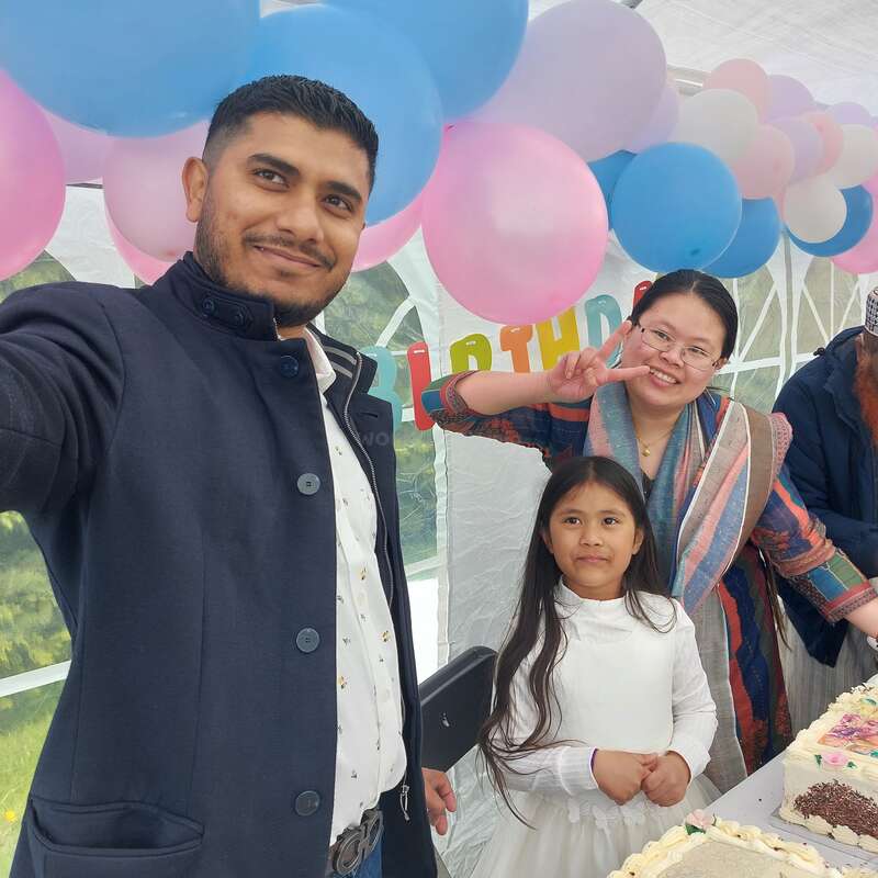 Un homme prend un selfie avec une femme et une petite fille lors d'une fête d'anniversaire. Des ballons colorés et des gâteaux créent une ambiance joyeuse et festive.