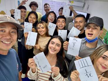 Un groupe d'élèves souriants et leur professeur montrent fièrement des feuilles couvertes de caractères chinois manuscrits dans une salle de classe, célébrant leurs progrès dans l'apprentissage de la langue.