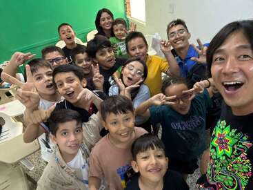 Un groupe joyeux d'enfants et d'adultes pose ensemble dans une salle de classe, souriant et faisant le signe de la paix, profitant clairement d'un moment amusant, convivial et animé.