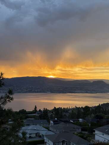 Um deslumbrante pôr do sol dourado ilumina o céu acima de montanhas tranquilas, um lago calmo e uma vizinhança tranquila, criando uma cena de paisagem natural pacífica e pitoresca.
