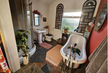 Dieses vielseitige Gemeinschaftsbad hat eine Badewanne mit Löwenfüßen, eine moderne Dusche, Topfpflanzen, bunte Teppiche, verzierte Spiegel, Fliesenboden und dekorative Holzfensterläden für natürliches Licht.