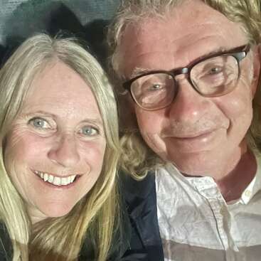 Un hombre y una mujer sonrientes, ambos con el pelo claro, se toman juntos un primer plano de un selfie. El hombre lleva gafas y camisa blanca. Parecen felices.