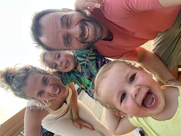 La imagen muestra a una familia de cuatro miembros posando para un selfie, con dos adultos y dos niños, todos sonriendo y mirando a la cámara.