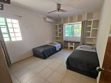 Dieses Zimmer verfügt über zwei Einzelbetten mit dunkler Bettwäsche, eingebaute Regale, geflieste Böden, einen Deckenventilator, eine Klimaanlage und große Fenster, die viel Tageslicht hereinlassen.