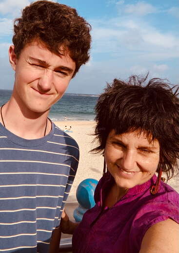 Das Bild zeigt einen jungen Mann und eine Frau, die für ein Selfie an einem Strand posieren, mit dem Meer und dem Himmel im Hintergrund.