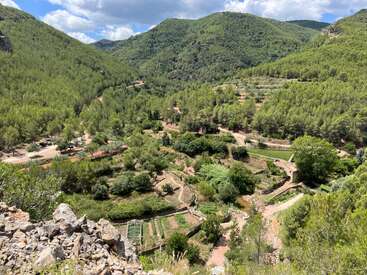 Vales verdejantes e colinas cobertas por uma densa floresta. Pequenos lotes agrícolas, caminhos sinuosos e uma lagoa aninhada em uma paisagem montanhosa e tranquila.