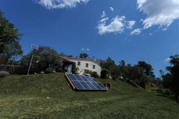 Une maison de campagne se dresse sur une colline herbeuse sous un ciel bleu. Des panneaux solaires sont installés sur la pente, soulignant le caractère durable d'un mode de vie hors réseau entouré par la nature.