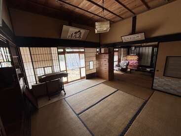 Esta imagem mostra um quarto de tatame japonês tradicional com portas shoji deslizantes, teto de madeira, cômoda, mesa baixa, futons empilhados e arte de caligrafia.