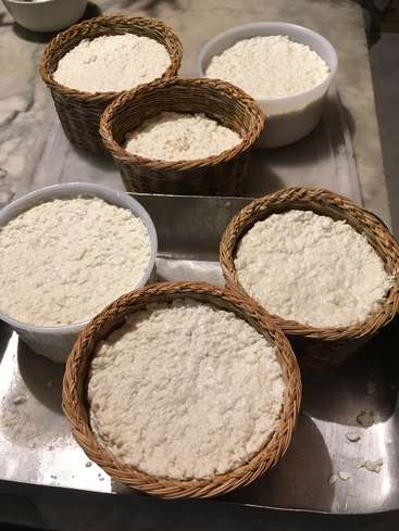 L'image montre cinq paniers de fromage blanc sur un plateau métallique, avec deux conteneurs de fromage en plastique à côté, sur un comptoir en marbre.