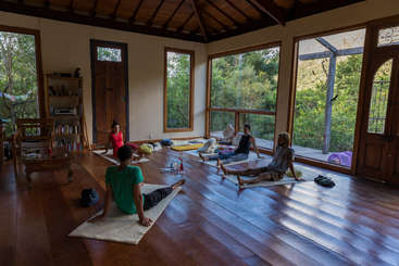 A imagem retrata um estúdio de ioga sereno com um grupo de pessoas sentadas no chão, cercadas por uma atmosfera pacífica, transmitindo uma sensação de tranquilidade e relaxamento.