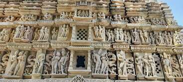 Das Bild zeigt komplizierte Steinmetzarbeiten an einer Tempelwand, die detaillierte menschliche Figuren, Gottheiten, Tänzer und Tiere darstellen und die alte indische Kunst und Handwerkskunst zeigen.