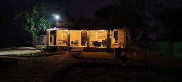 Ein gemütliches Haus leuchtet nachts warm und ist mit Lichterketten geschmückt. Umgeben von Bäumen und einem offenen Hof, schafft es in der Dunkelheit eine friedliche, einladende Atmosphäre.