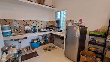 This image shows a small, cluttered kitchen with a refrigerator, gas stove, dishes, utensils, storage shelves, and a window providing natural light. Various supplies scattered around.