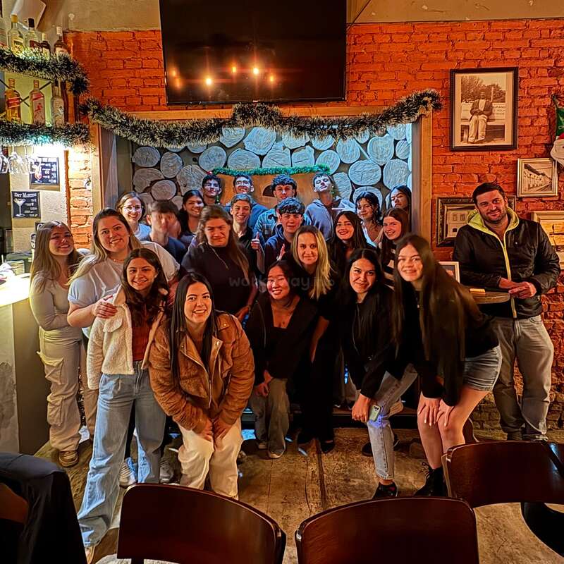 Un grupo de jóvenes adultos se reúnen en un acogedor bar con paredes de ladrillo, sonríen y posan juntos para una foto de grupo, derrochando alegría y calidez en un entorno festivo.