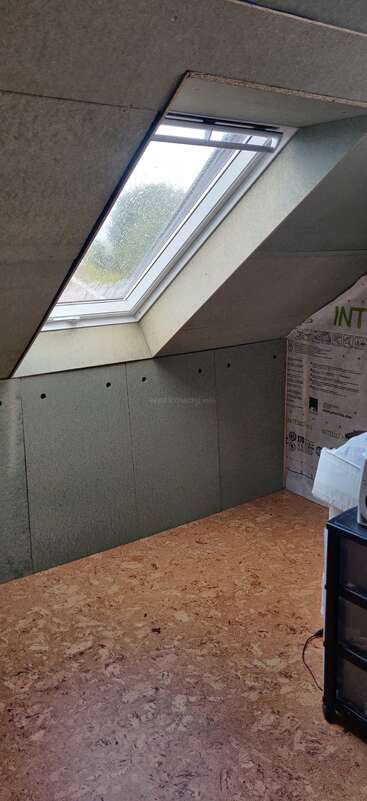 Cette photo montre une chambre mansardée en cours de rénovation, avec un plafond en pente doté d'une lucarne, un sol en liège et des matériaux d'isolation le long du mur.