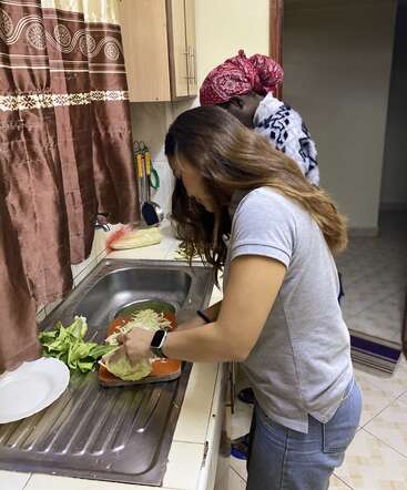 Zwei Frauen bereiten gemeinsam in einer Küche Gemüse zu. Die eine hackt Kohl an der Spüle, während die andere daneben steht, beide konzentriert auf das Kochen.
