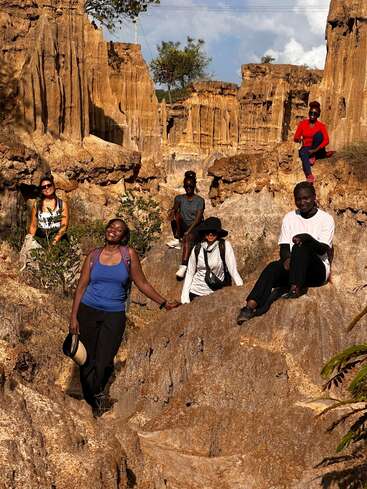 Un grupo de cinco personas posa alegremente entre escarpadas formaciones rocosas doradas bajo un cielo soleado, disfrutando de una pintoresca aventura al aire libre rodeados de espectaculares paisajes naturales y vegetación.