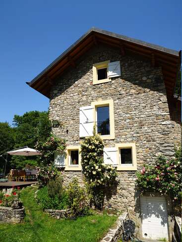 Cette charmante maison en pierre se distingue par ses moulures jaunes, ses volets blancs, ses rosiers grimpants et son jardin luxuriant. À proximité se trouve une terrasse confortable équipée d'une table et d'un parasol.