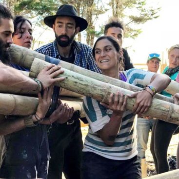 The image depicts a group of people working together to construct a structure made of bamboo, with a focus on teamwork and collaboration.