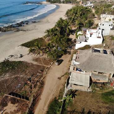 Aerial view of a tropical beach, palm trees lining a sandy road, a few houses with thatched roofs, clear blue ocean waves, peaceful and serene atmosphere.