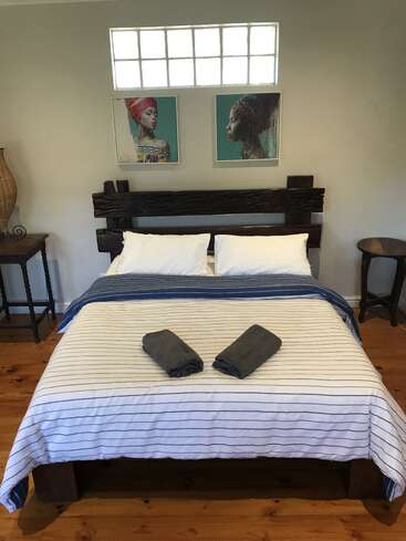 Ein ordentlich gemachtes Bett mit weiß-blau gestreifter Bettwäsche, zwei gefalteten Handtüchern, einem Kopfteil aus Holz, Nachttischen und zwei Porträts darüber, in einem gemütlichen Zimmer.