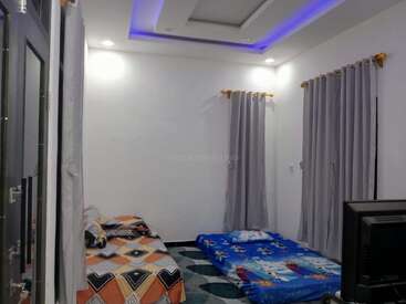 Cette image montre une chambre à coucher simple et moderne avec un lit simple, un matelas sur le sol, des rideaux gris, une télévision et des lumières bleues au plafond.