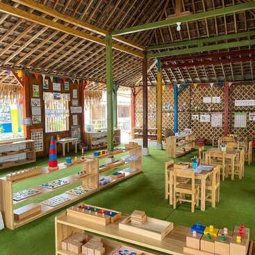 This image shows a colorful, open-air classroom with wooden furniture, educational materials, learning toys, decorated walls, student artwork, and bright, inviting spaces for young children.