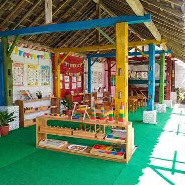This image shows a colorful classroom with wooden furniture, educational toys, learning materials, bright posters, and cheerful decorations, creating an inviting and playful learning environment for children.
