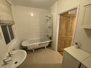 Se trata de un cuarto de baño limpio y bien iluminado, con una bañera independiente, una ducha empotrada en la pared, un lavabo, una puerta de madera, un armario, un espejo y una ventana con persianas.