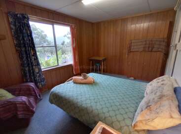 This cozy room features wood-paneled walls, a large window with outdoor views, a double bed with a green cover, a table, and simple decor.