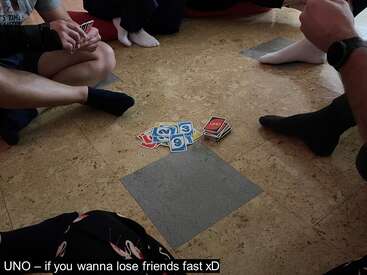 Un grupo de personas se sienta en el suelo en círculo, jugando al UNO. Las cartas están esparcidas por el centro. El pie de foto bromea sobre perder amigos rápidamente.