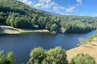 Un río sereno serpentea a través de frondosos bosques verdes y campos abiertos bajo un cielo azul claro salpicado de nubes esponjosas, rodeado de colinas lejanas y tranquilidad.
