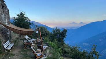 The image depicts a serene outdoor setting with a table and chairs, surrounded by trees and a body of water, evoking a sense of tranquility and relaxation. The scene is peaceful and idyllic.