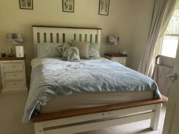 Dieses gemütliche Schlafzimmer verfügt über ein ordentlich gemachtes Bett mit blauer Bettwäsche, passende Kissen, zwei Nachttische mit Lampen, Wandkunst, helle Vorhänge und natürliches Licht.
