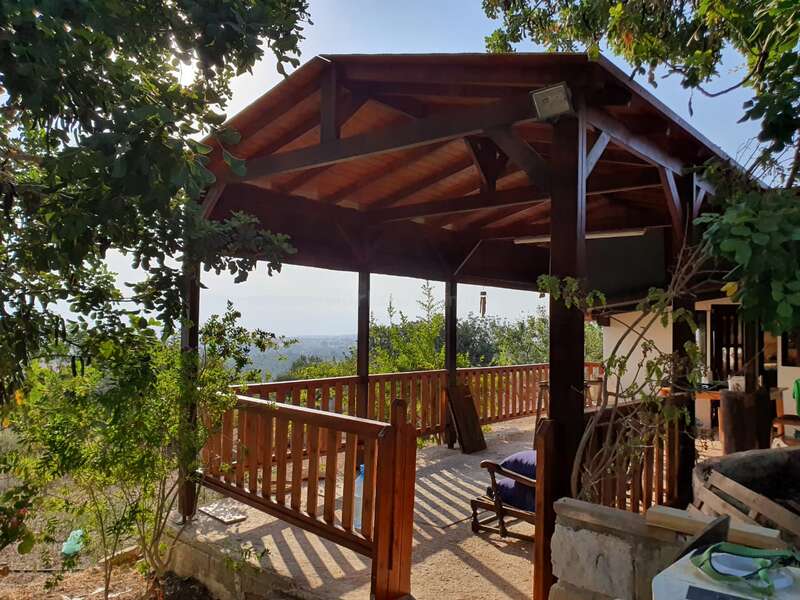 Ein hölzerner Pavillon mit einem spitzen Dach ist von üppigem Grün umgeben. Das Sonnenlicht fällt durch die Bäume und schafft einen friedlichen Sitz- und Entspannungsbereich im Freien.