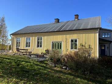 The image depicts a charming yellow house with a gray roof, surrounded by a lush green lawn and a serene blue sky.