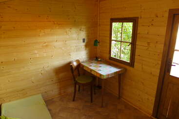 O interior desta aconchegante cabana de madeira tem uma mesinha com uma toalha xadrez, uma cadeira verde, uma janela com vista e uma porta de madeira.
