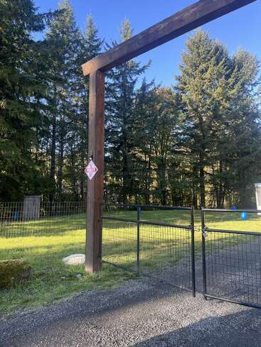 A metal gate with a lock is attached to wooden posts under a large wooden archway. There’s a "Private Property" sign and tall trees in the background.