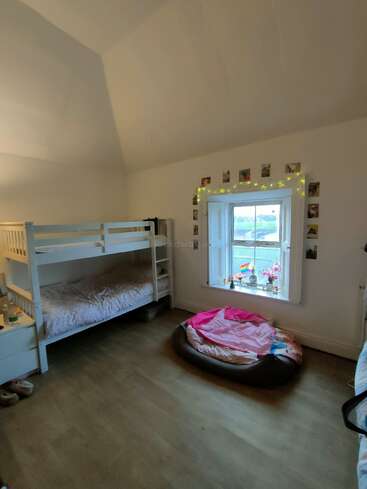 Une chambre confortable avec des lits superposés, un grand lit pour animaux, une fenêtre décorée avec des plantes, des guirlandes lumineuses, des photos au mur, un sol en bois et un éclairage doux.