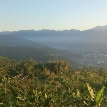 The image depicts a serene mountainous landscape with lush vegetation, a bridge, and distant mountains, set against a clear blue sky.