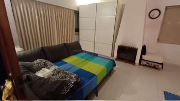 This cozy room features a pull-out sofa bed with colorful bedding, a white wardrobe, curtains, a wall clock, a fireplace, and tiled flooring, creating comfort.