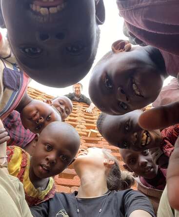 La imagen muestra a un grupo de niños y un adulto tomándose un selfie, con el adulto tumbado en el suelo y los niños rodeándole.