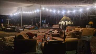 Un acogedor salón al aire libre bajo un toldo, con sofás, cojines, alfombras, luces de cuerda y una carpa. Un ambiente acogedor para socializar o relajarse por la noche.