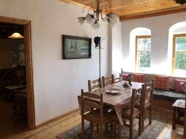 This cozy dining area features wooden furniture, a table set for a meal, large bright windows, a chandelier, wall art, a coat rack, and decorative pillows.