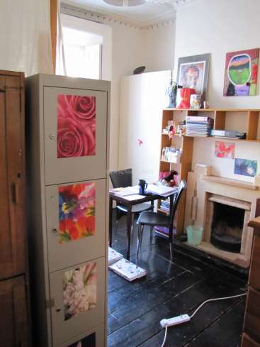 The image depicts a cozy room with a fireplace, a desk, and a tall cabinet adorned with floral artwork. The room is well-lit and features a window.