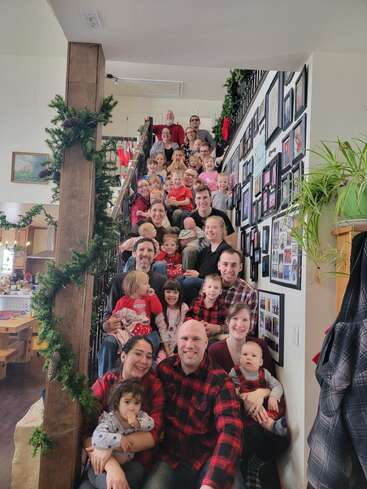 Une famille nombreuse et heureuse se rassemble dans un escalier décoré de guirlandes et sourit pour une photo de groupe. Enfants et adultes posent ensemble, créant une scène chaleureuse et festive.
